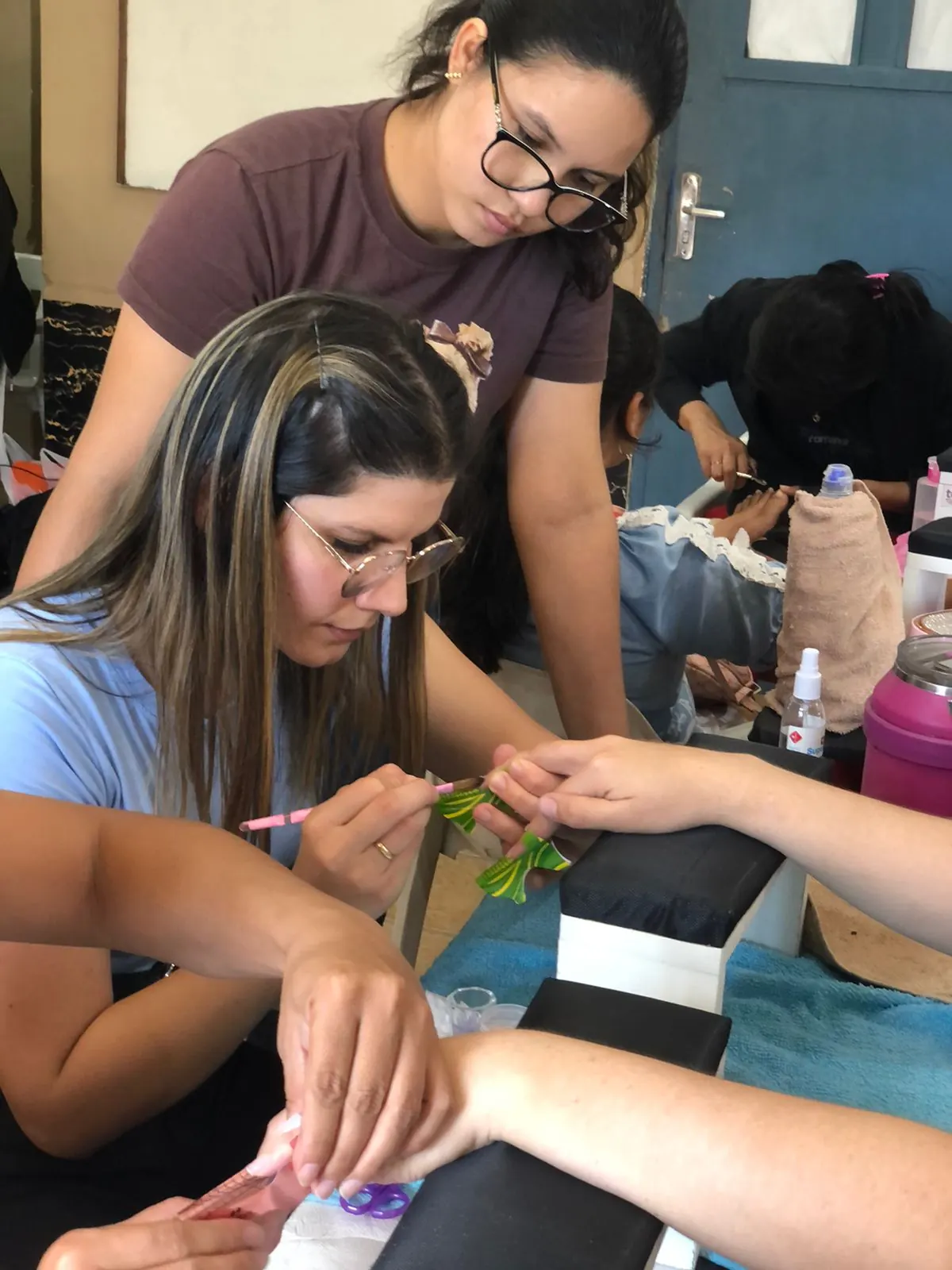 Clase práctica de manicura con instructora acompañando alumnas